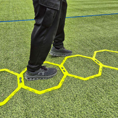 Person standing on a yellow hexagonal grid on a green artificial turf field.